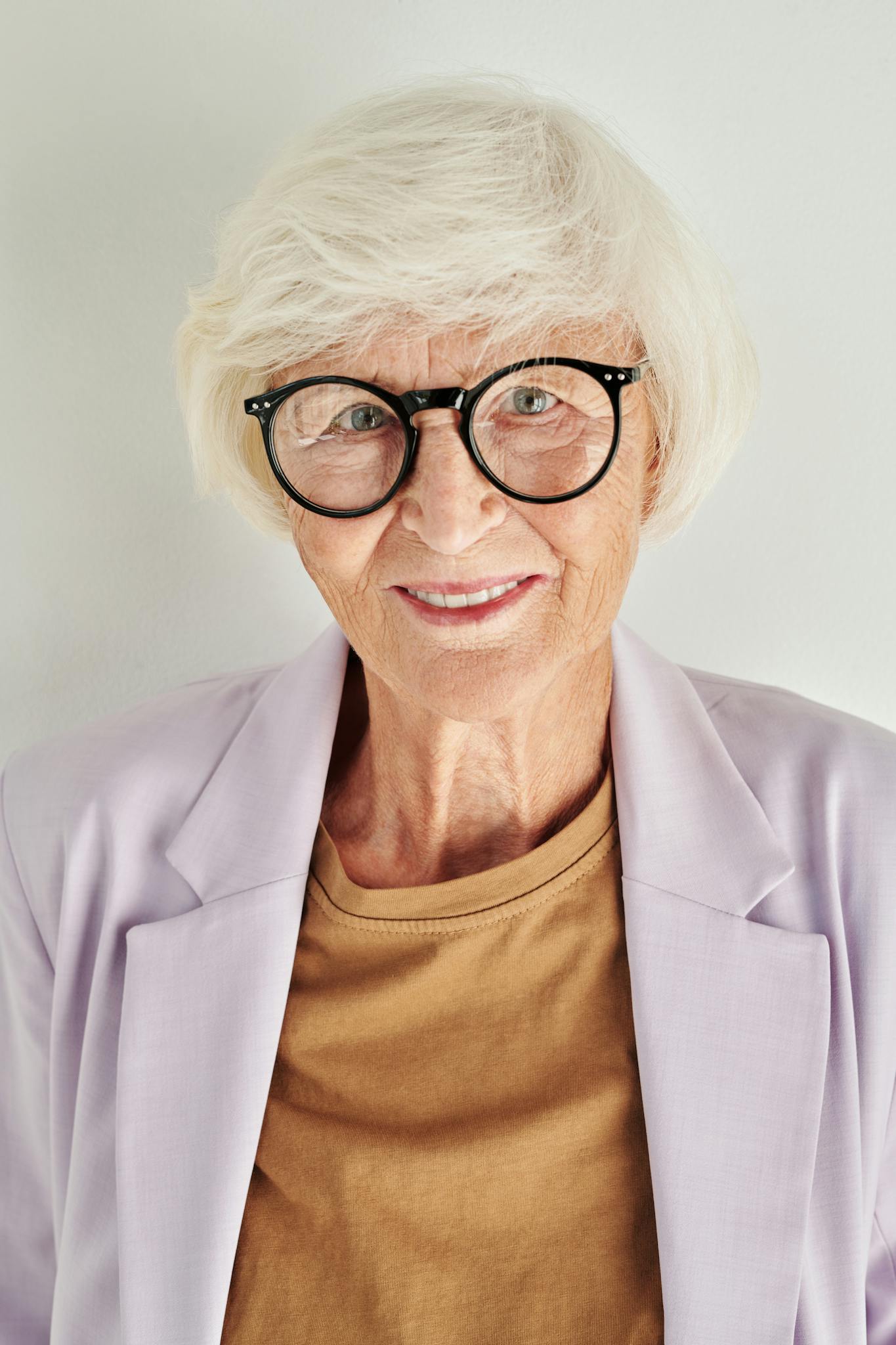 Elegant senior woman with white hair and glasses smiling confidently in a stylish blazer.