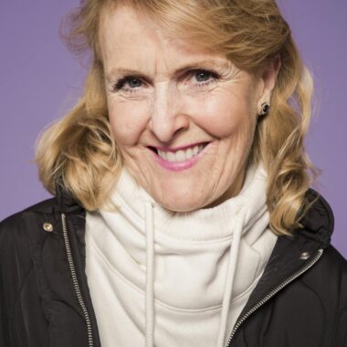 Portrait of a smiling senior woman in casual fashion against a purple background, exuding elegance and warmth.