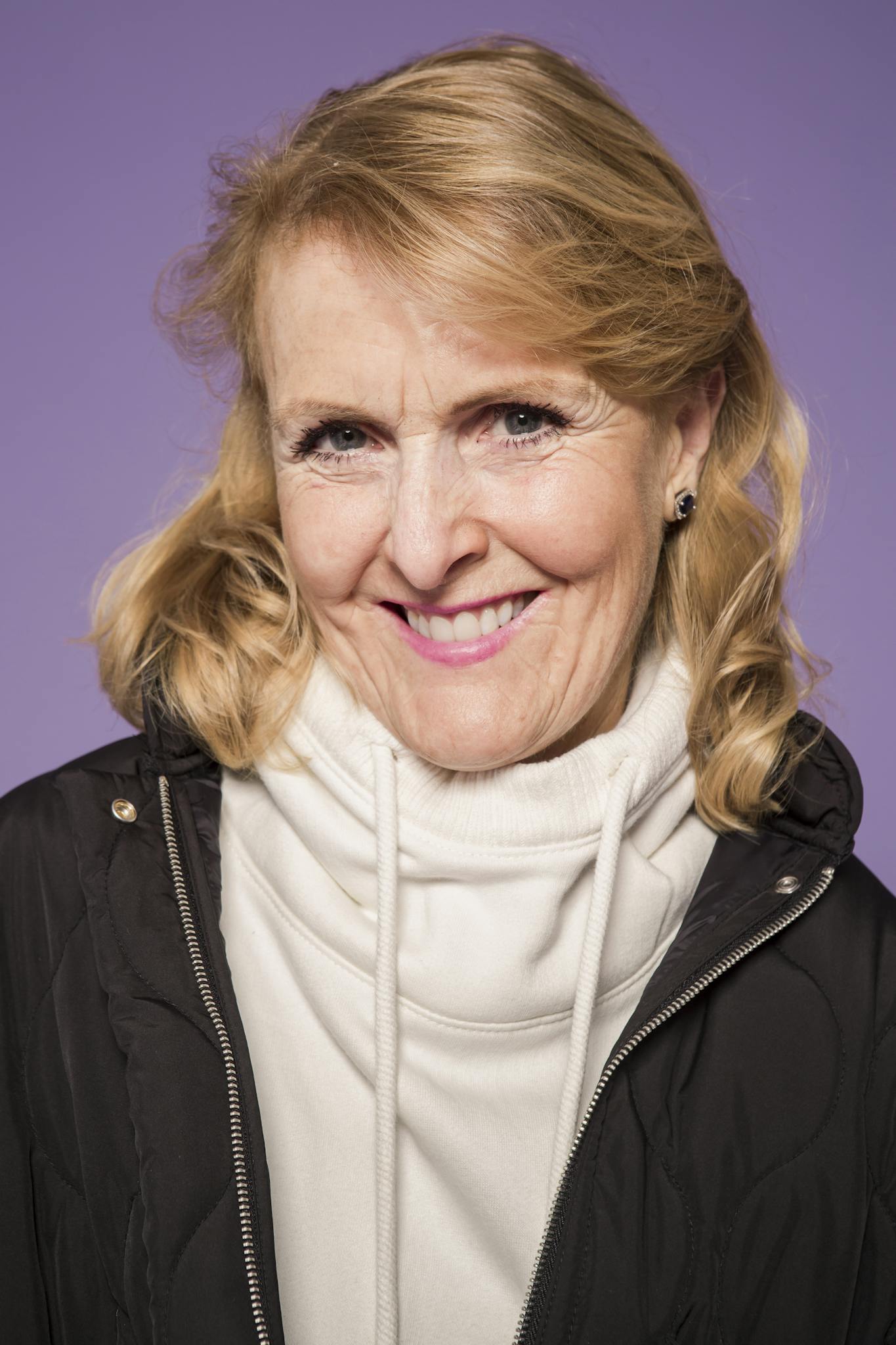 Portrait of a smiling senior woman in casual fashion against a purple background, exuding elegance and warmth.