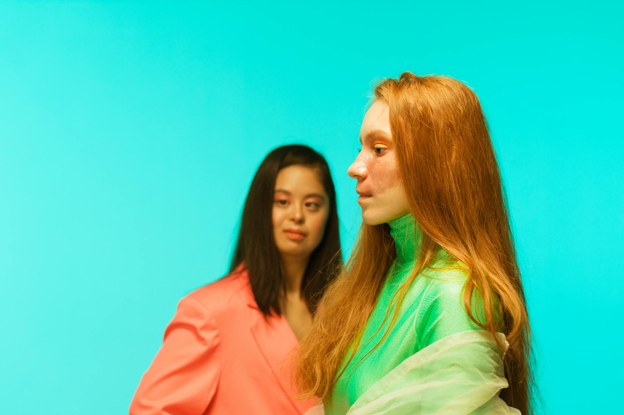 Trendy women modeling stylish outfits against a vibrant teal background, showcasing fashion and diversity.